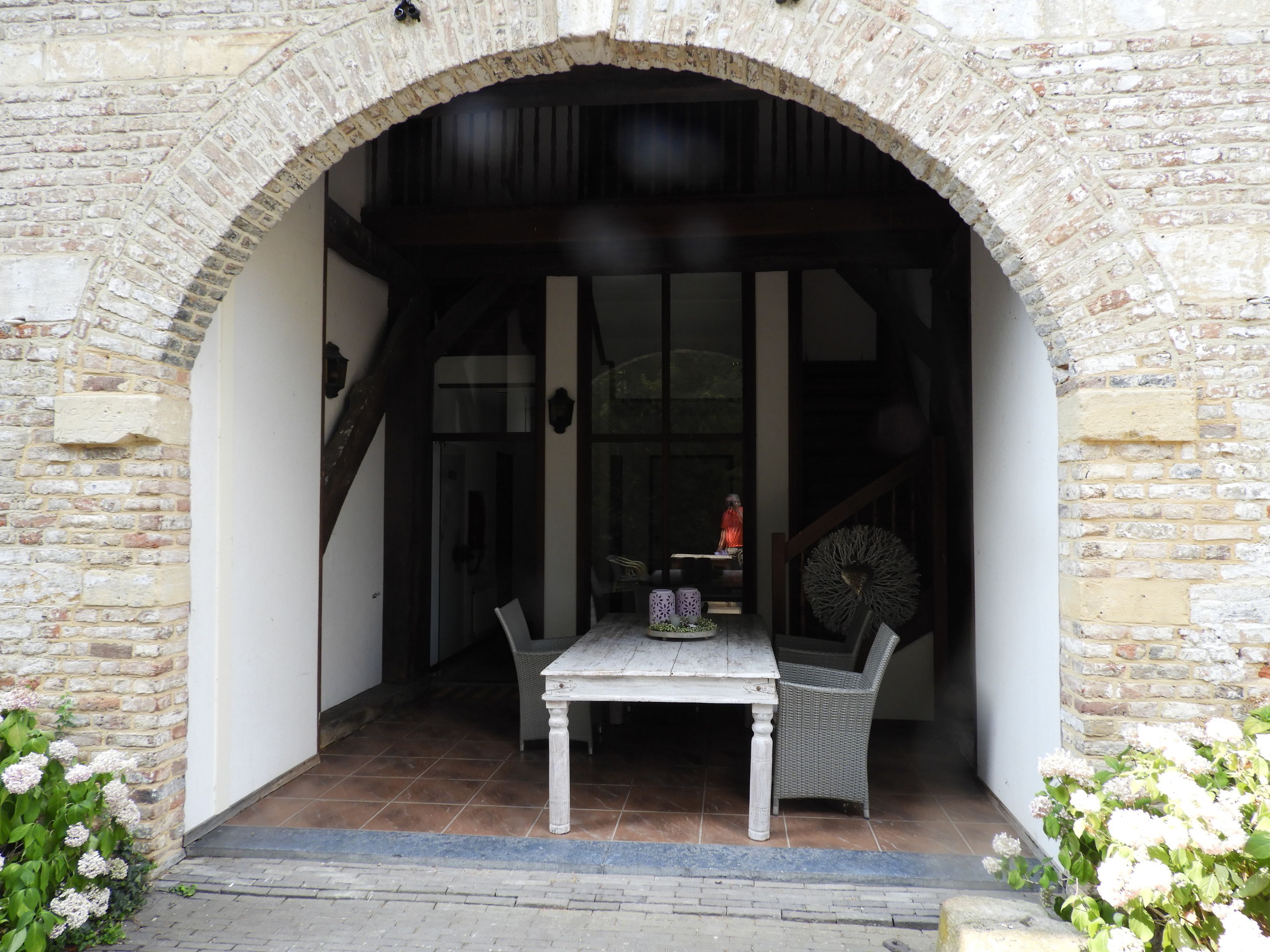 An arched stone entrance to a building with a table and chair outside.