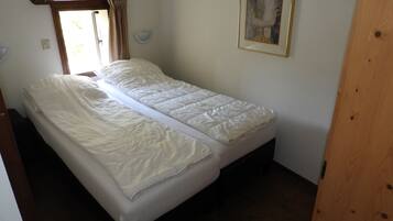 Una habitación pequeña con cama individual, suelo de madera, ventana con cortinas e imagen enmarcada en la pared.