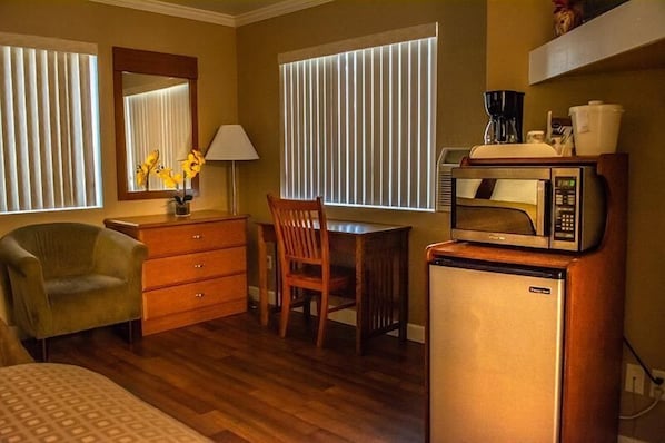 Quarto de hotel compacto com escrivaninha de madeira, uma cadeira, um pequeno frigorífico e micro-ondas.