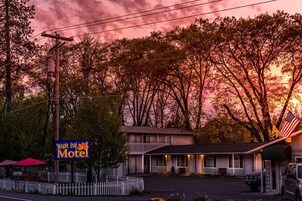 Um motel com uma placa, área de estacionamento cercada e um edifício com varanda.