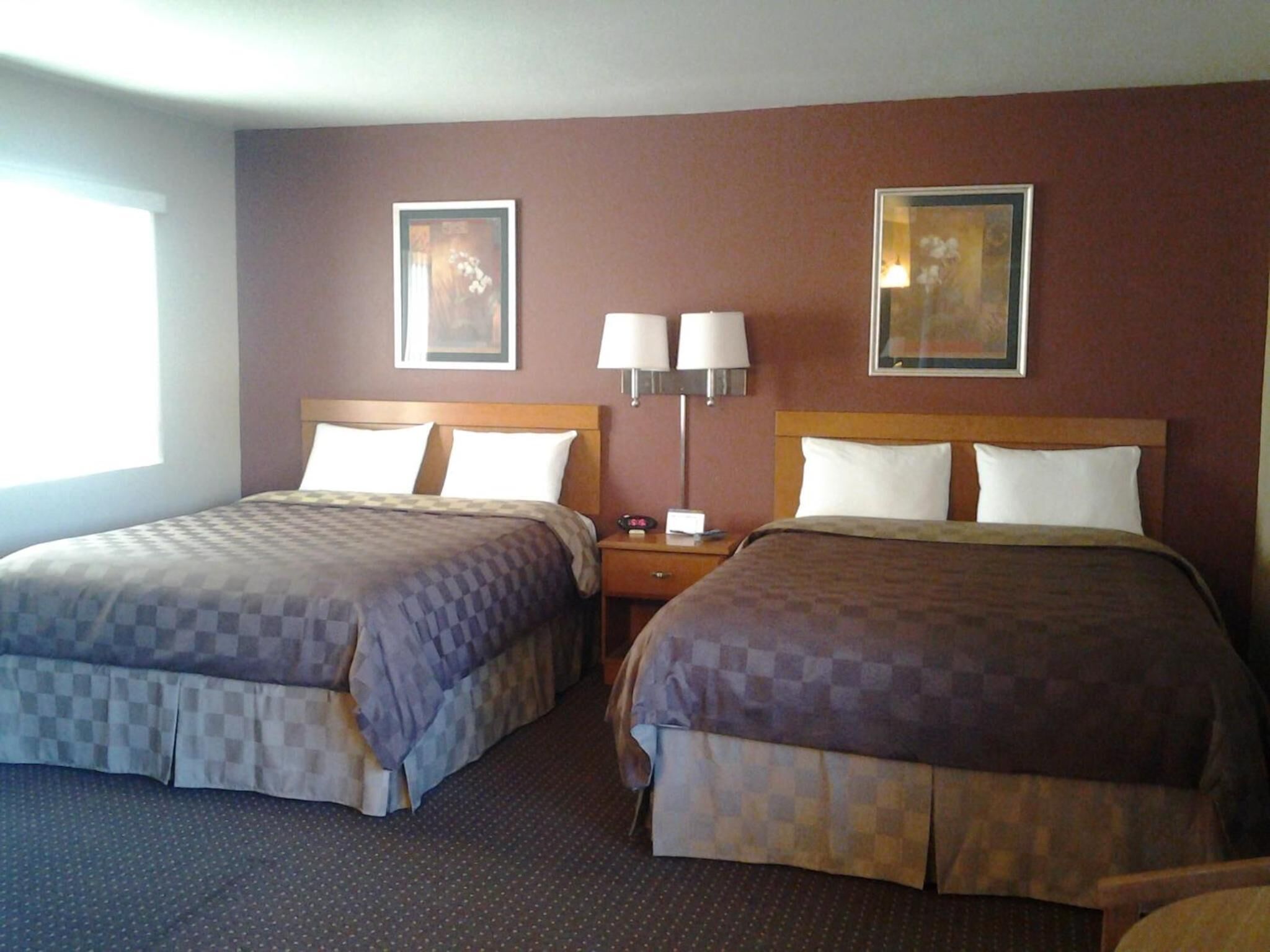 A hotel room with two beds, a nightstand, wall-mounted lamps, and framed artwork.