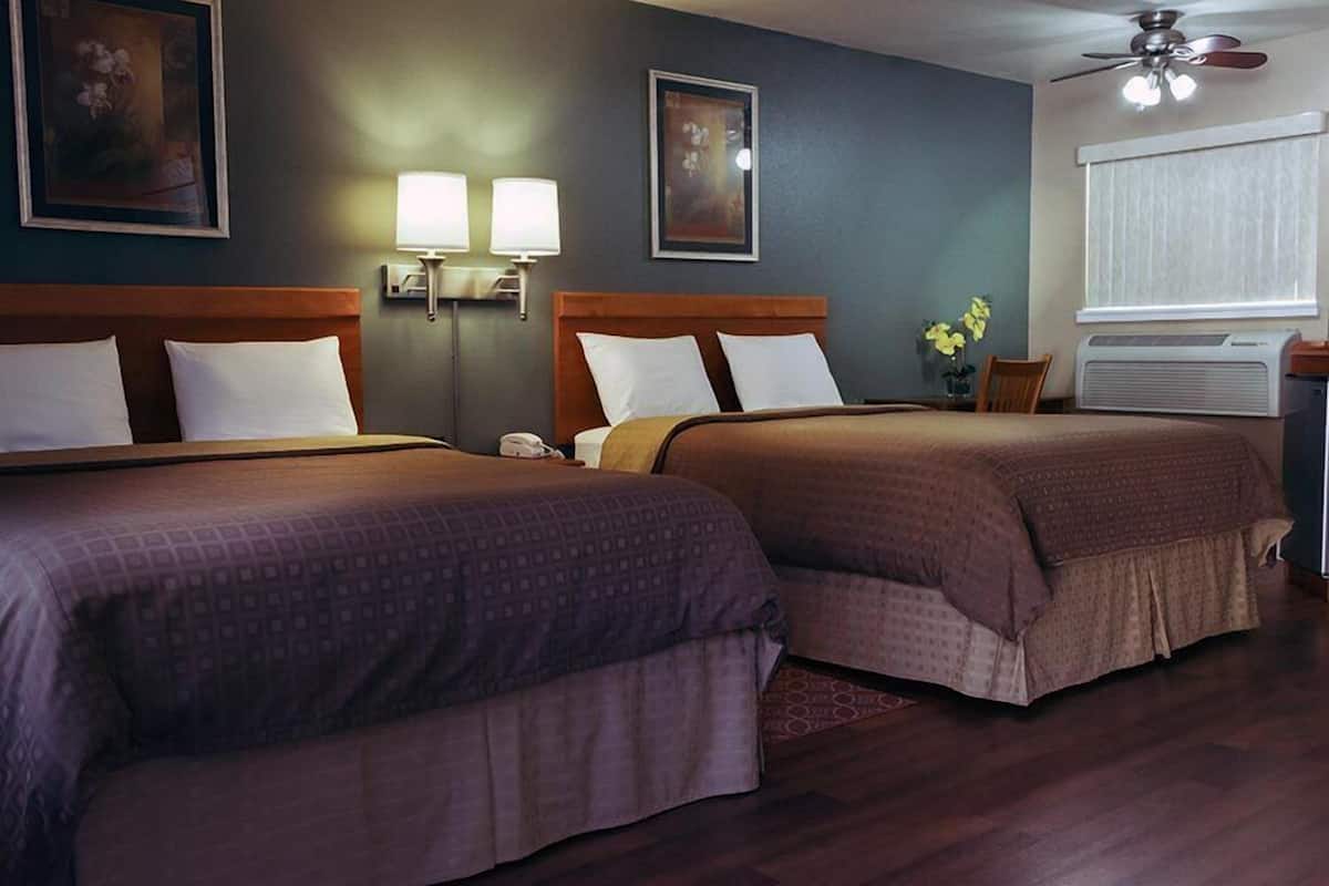 A hotel room with two beds, a ceiling fan, wall-mounted lamps, and an air conditioning unit.
