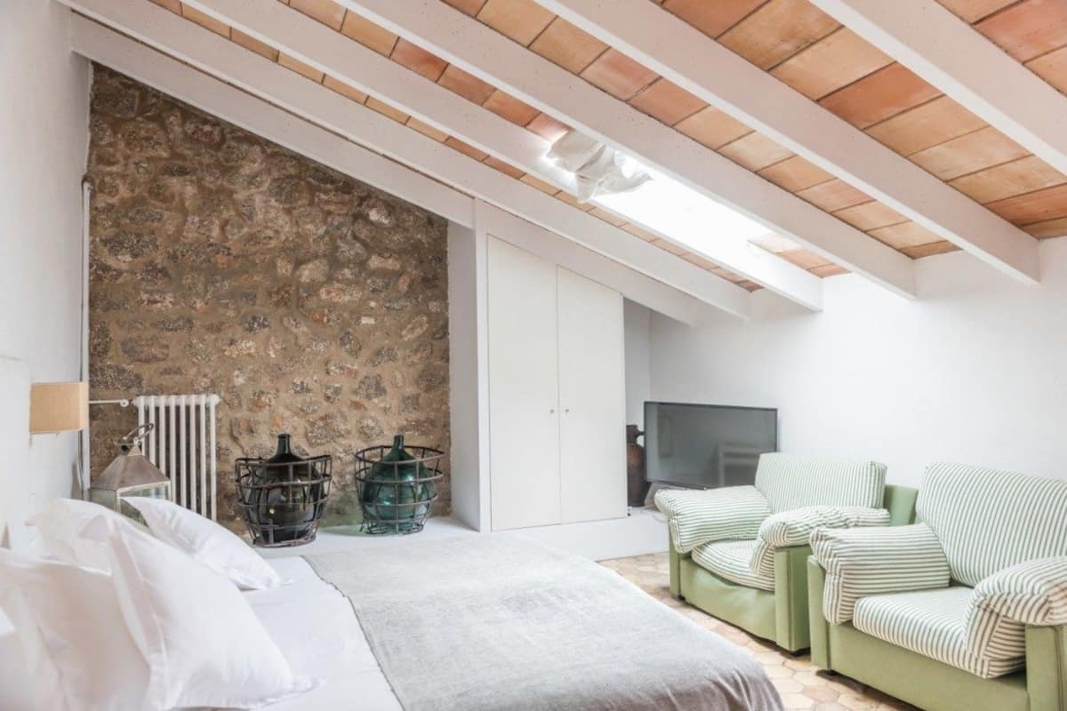A bedroom with a stone wall, a bed, a TV, and green striped chairs.