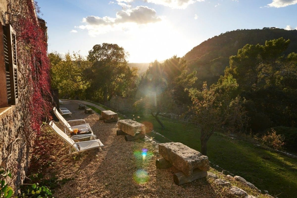 A courtyard with stone seating, a grassy area, and a view of a hilly landscape.