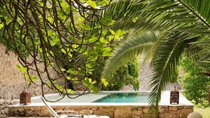 A poolside area with lounge chairs, a stone wall, and a palm tree. - Hotel Mirabó De Valldemossa (Valldemossa)