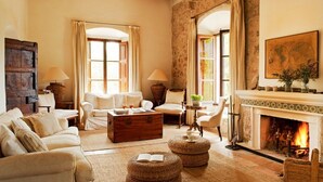 A cozy living room with a fireplace, comfortable seating, and a rustic stone wall. - Hotel Mirabó De Valldemossa (Valldemossa)