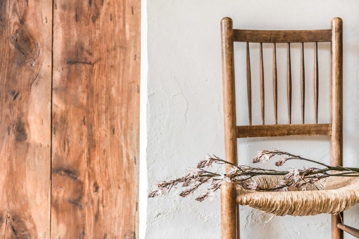 Una silla de madera rústica con asiento tejido y pared de superficie texturizada.