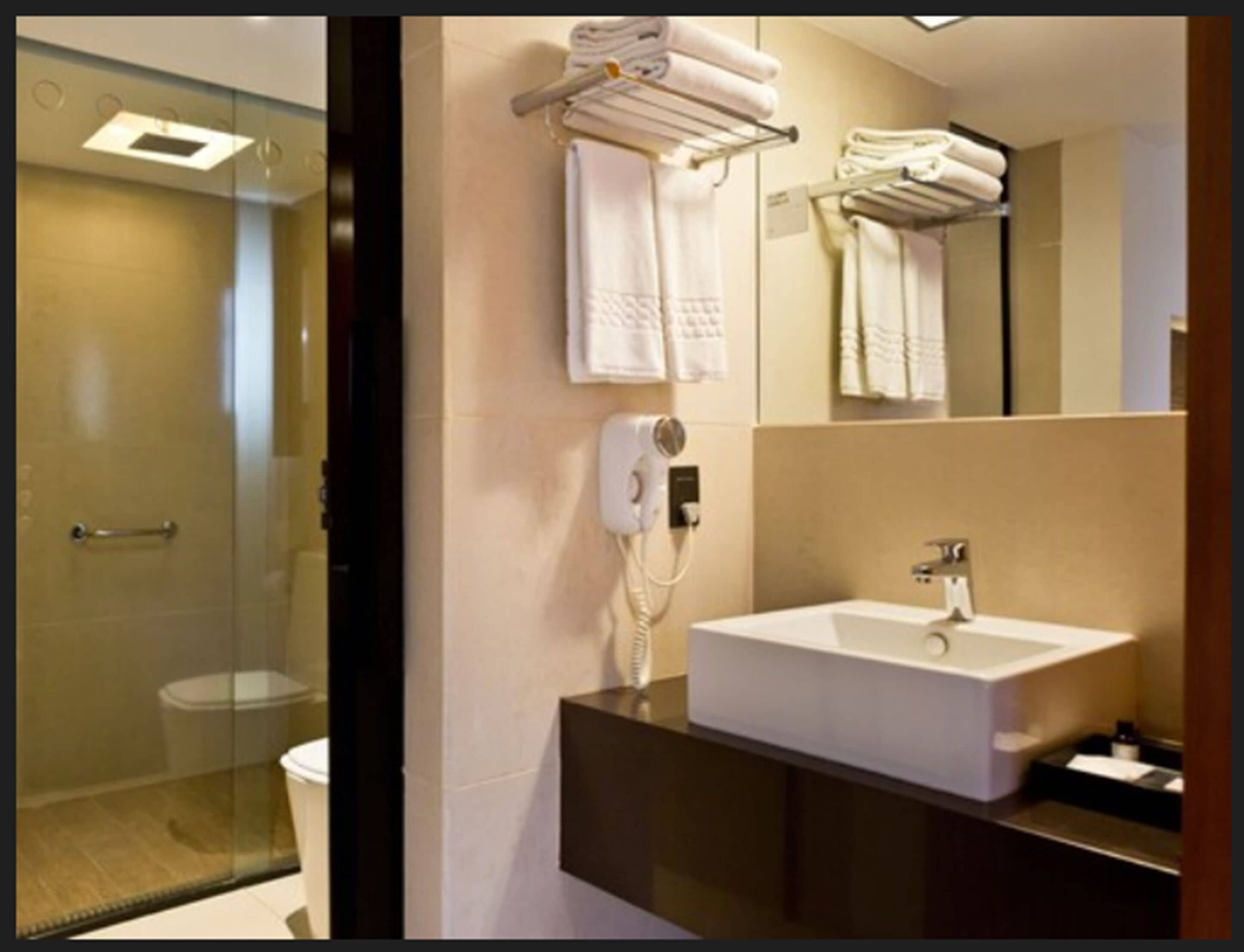 A modern bathroom with a glass shower enclosure, a white sink, and a towel rack with neatly folded towels.