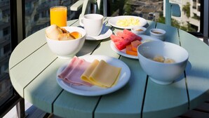 A balcony table with breakfast items, a chair, and a view of a cityscape with a prominent mountain. - Ritz Hotel Leblon (Rio de Janeiro)