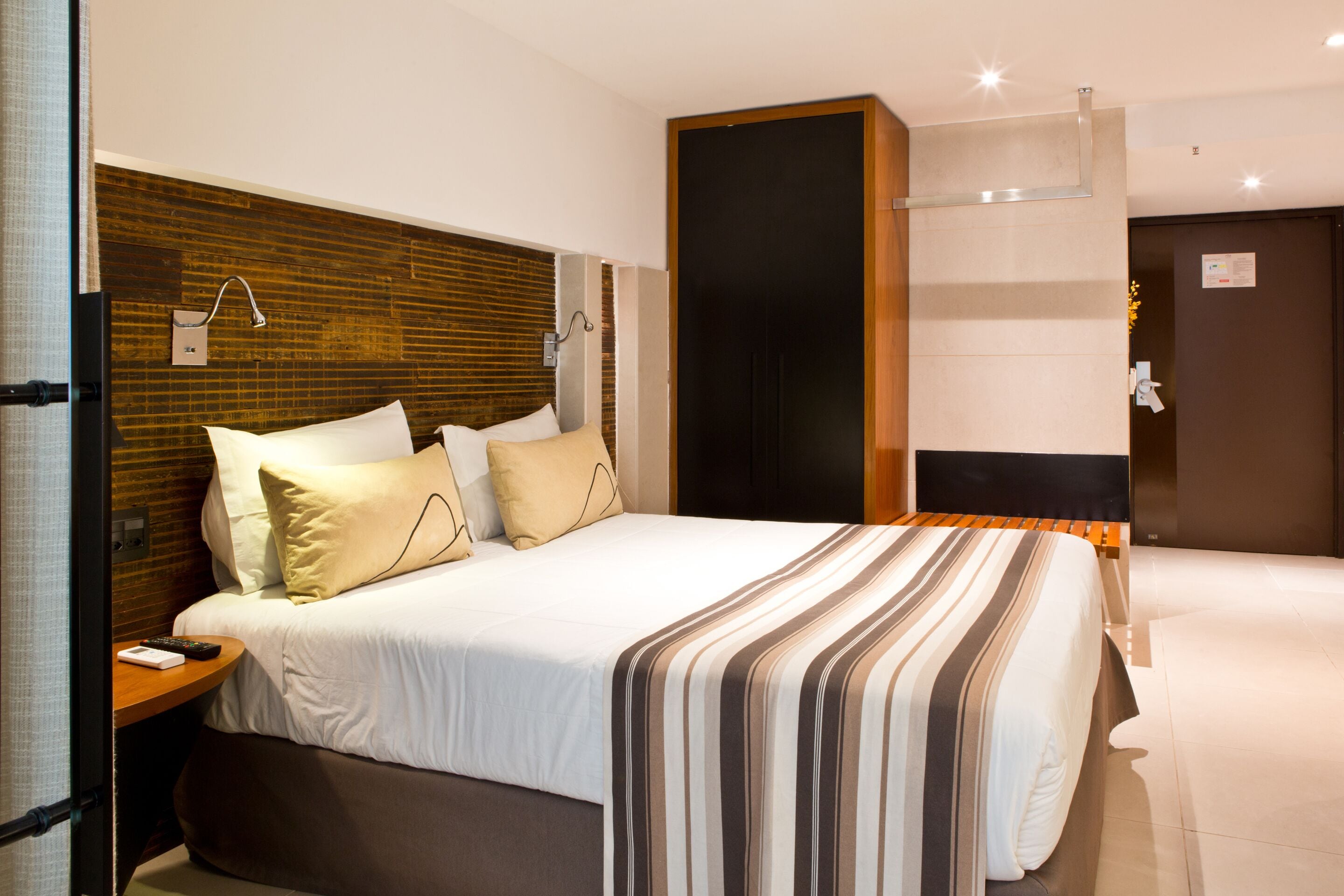 A modern hotel room with a large bed, a wooden headboard, and a nightstand with a remote control.