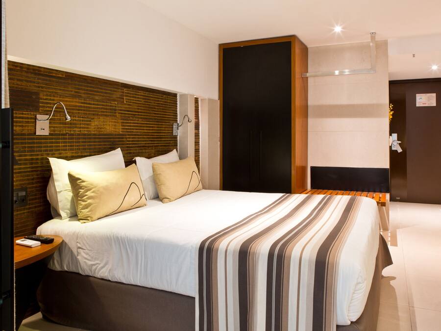 A modern hotel room with a large bed, a wooden headboard, and a nightstand with a remote control.