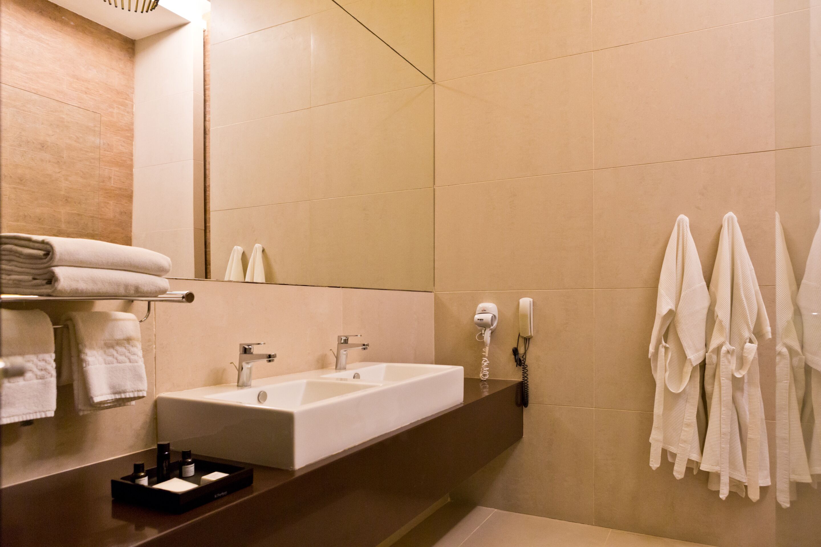 A modern bathroom with a large sink, a mirror, and a towel rack with multiple towels.