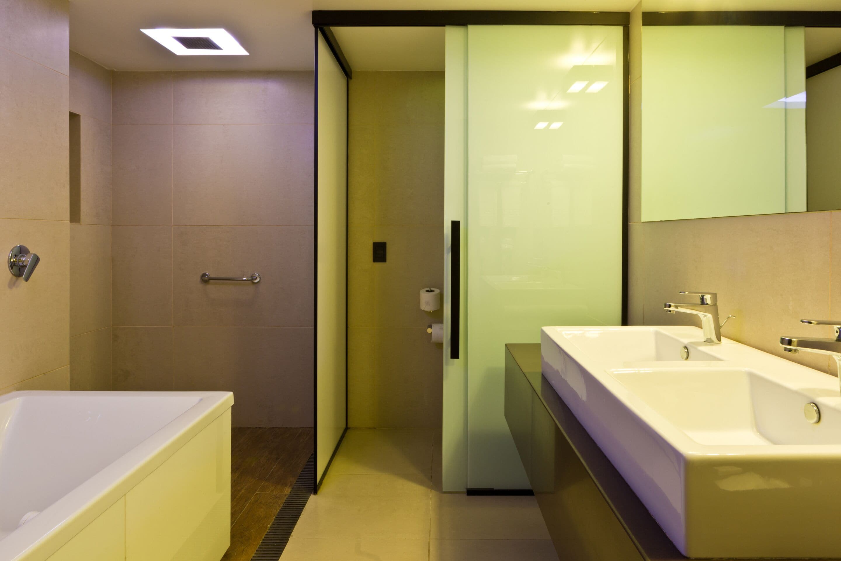 Un baño moderno con bañera, dos lavamanos y mampara de cristal.