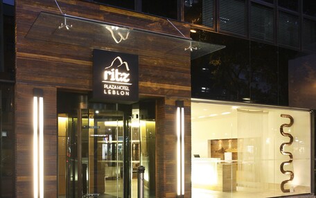 El exterior del Hotel Ritz Plaza, con un diseño moderno, que cuenta con una entrada de cristal y señalización iluminada.