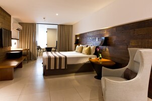 A modern hotel room with a large bed, a desk, a chair, and a TV.