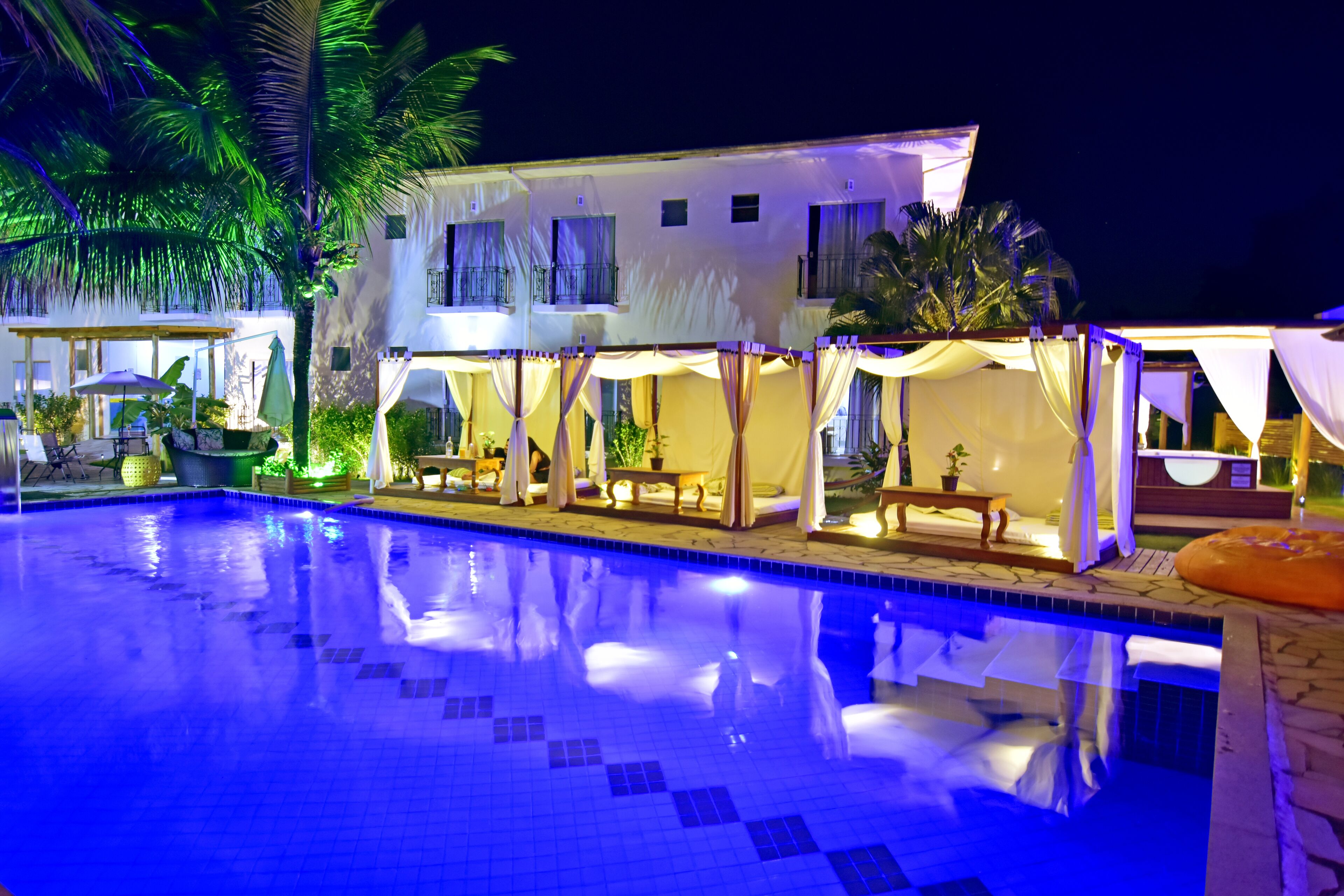 Una piscina con borde de azulejos, rodeada por una zona exterior cubierta con asientos y sombrillas.