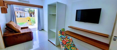 Una sala de estar moderna con un sofá marrón, un sillón colorido, un televisor de pantalla plana montado en la pared y un ventanal con vistas al exterior.