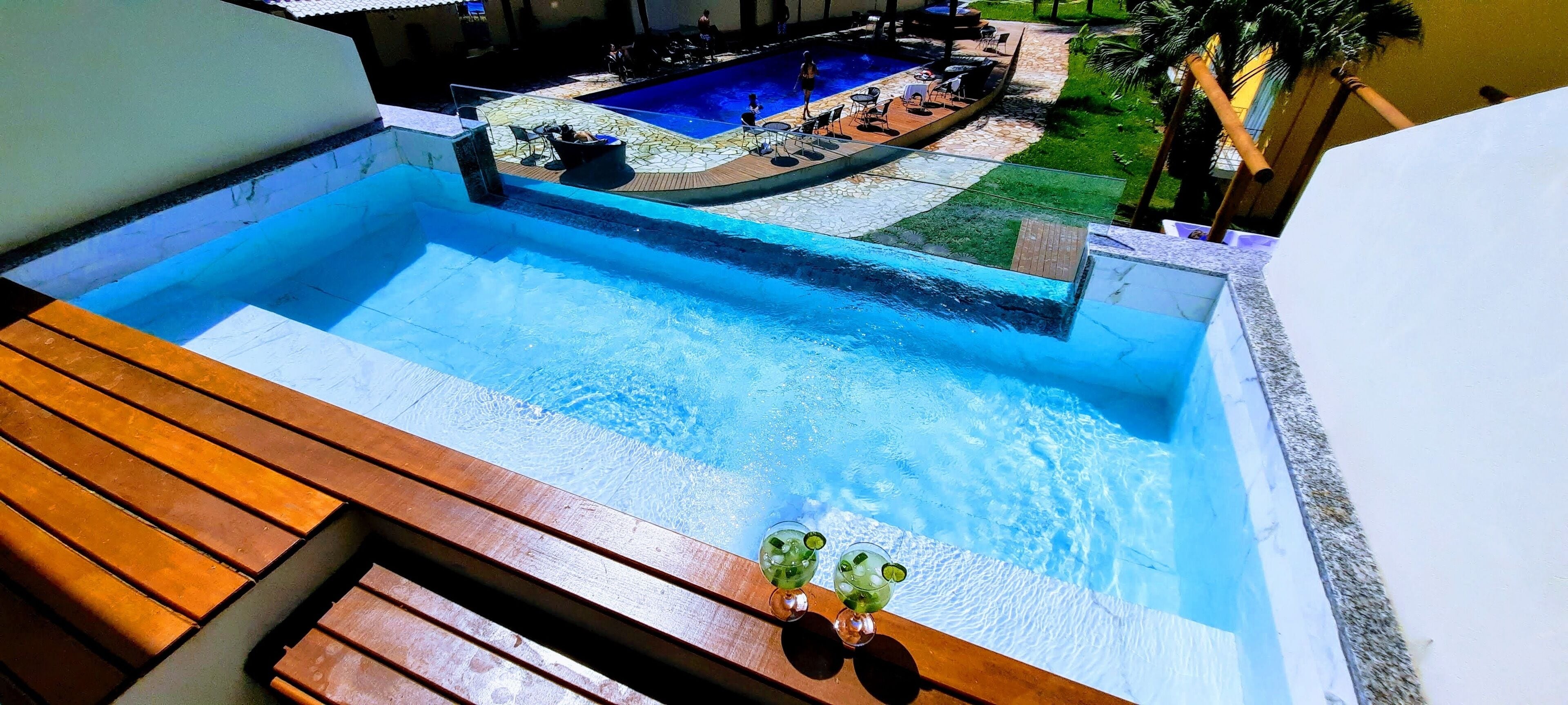 A swimming pool with a wooden deck and lounge chairs, surrounded by a landscaped garden and a building.