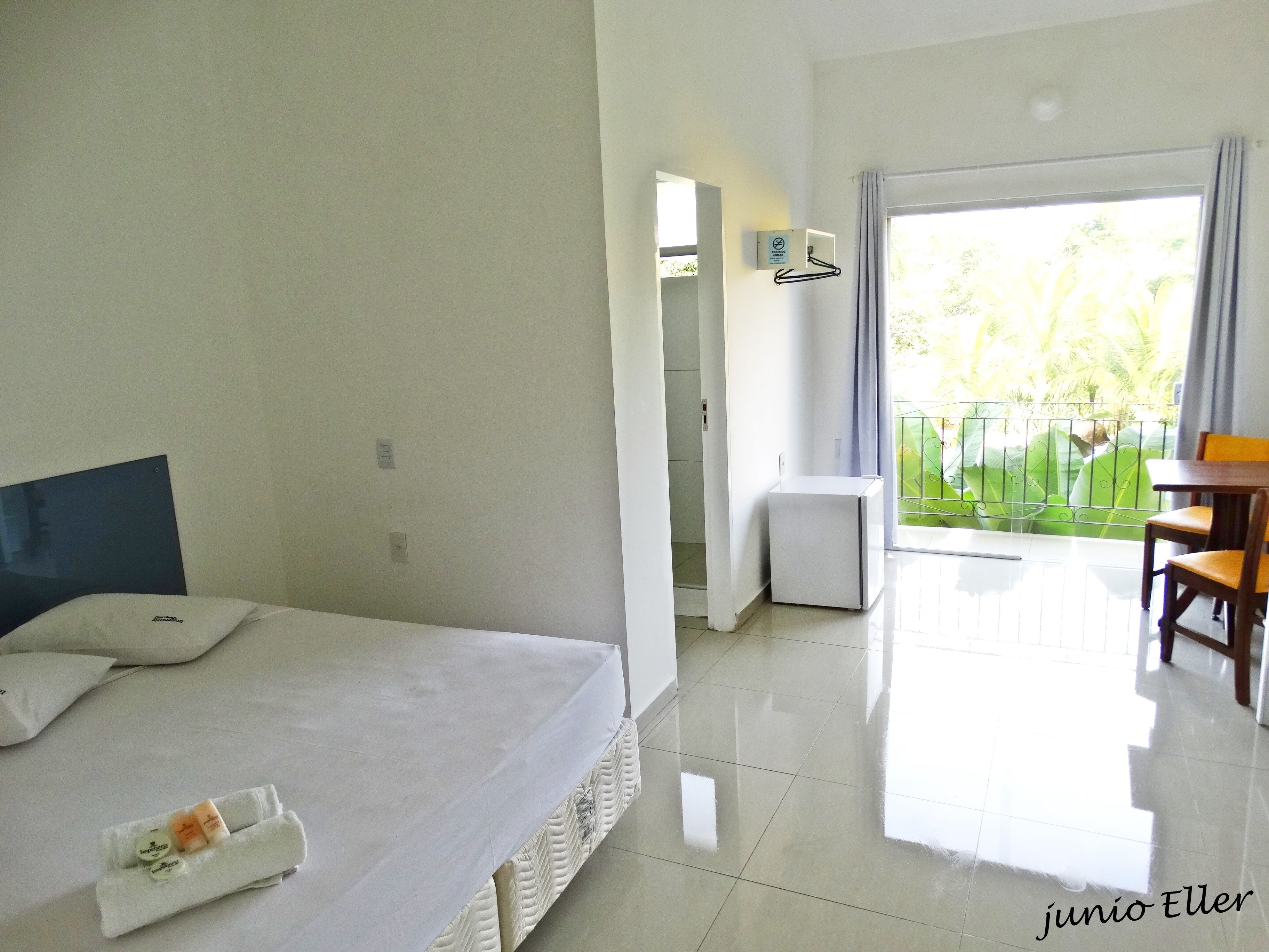 Habitación de hotel con cama, una mesita, una silla, un balcón con vistas a zonas verdes y una ventana.