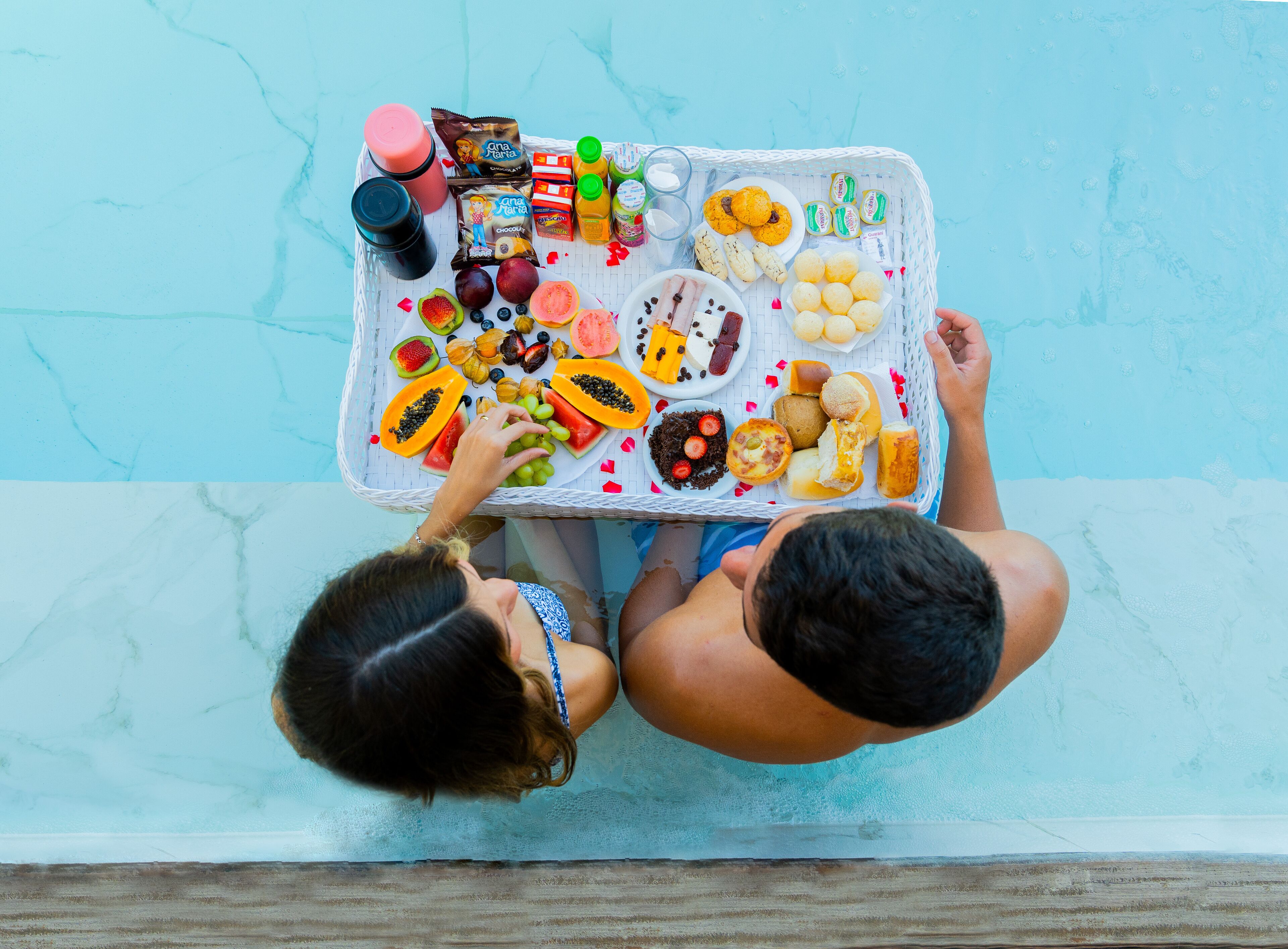 A poolside table with various snacks and drinks, including fruits, cookies, and bottled beverages.