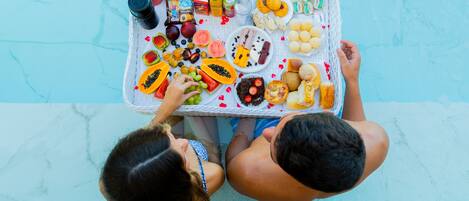 A poolside table with various snacks and drinks, including fruits, cookies, and bottled beverages.