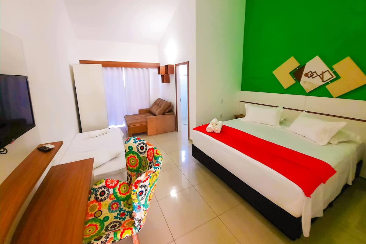 A hotel room with a bed, a sofa, a TV, and a colorful chair.