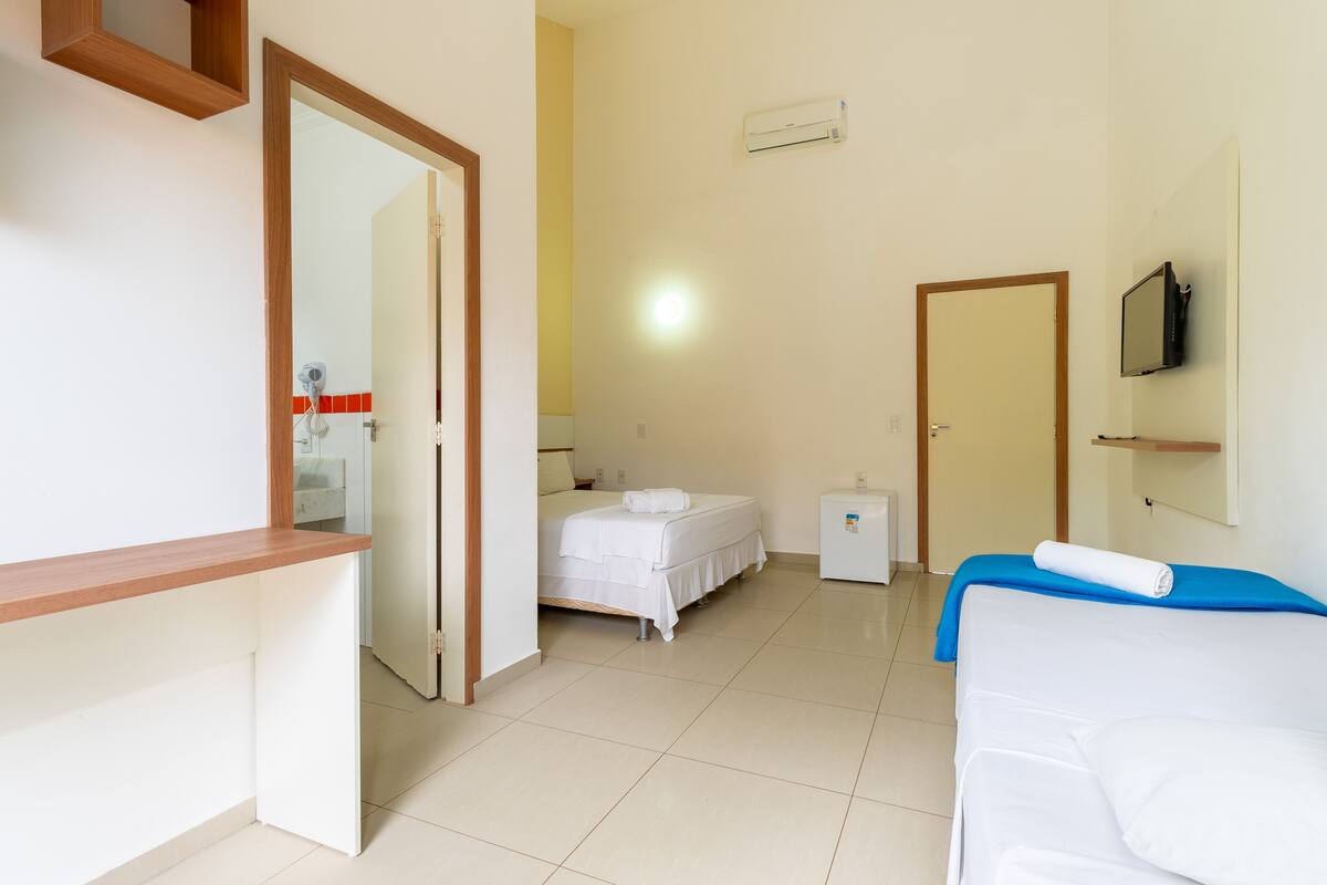 Habitación de hotel con cama, escritorio, televisor y baño visible a través de una puerta abierta.