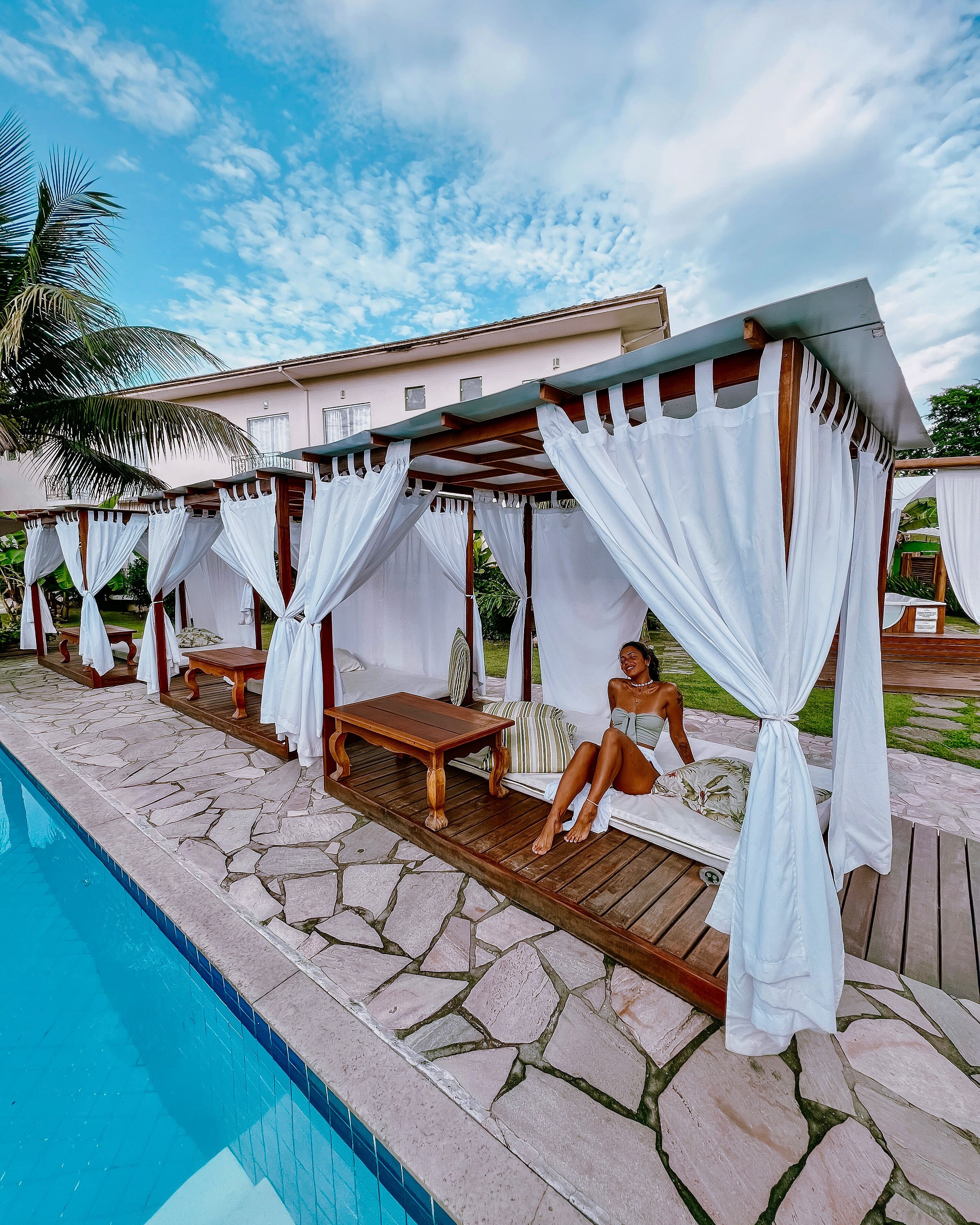 A poolside area with a covered seating area, stone flooring, and a pool.