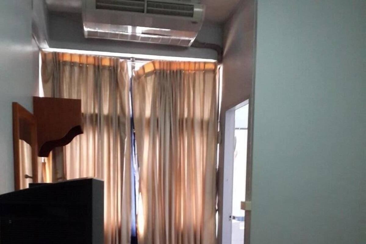 A hotel room with a bed, a desk with a television, curtains, a waste bin, and an air conditioning unit.