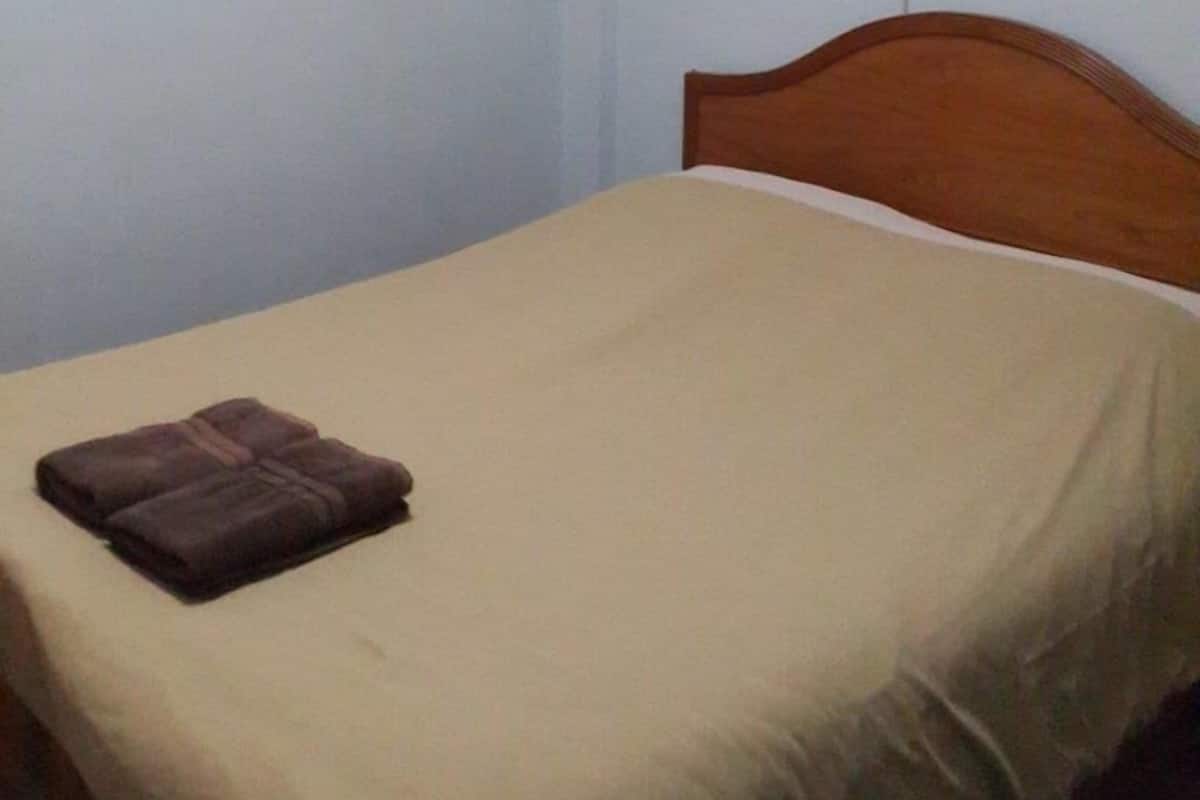 A single bed with a wooden headboard in a room with plain white walls.