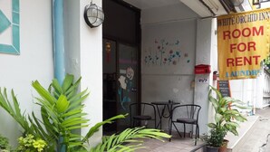 A hotel entrance with a 'Room for Rent' sign, outdoor seating, and potted plants. - White Orchid Inn (Bangkok)