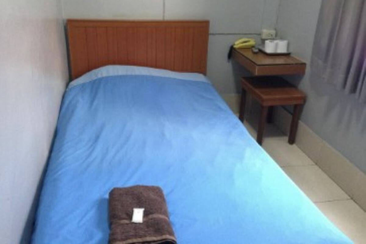 A single bed with a blue mattress and a wooden headboard in a small room.