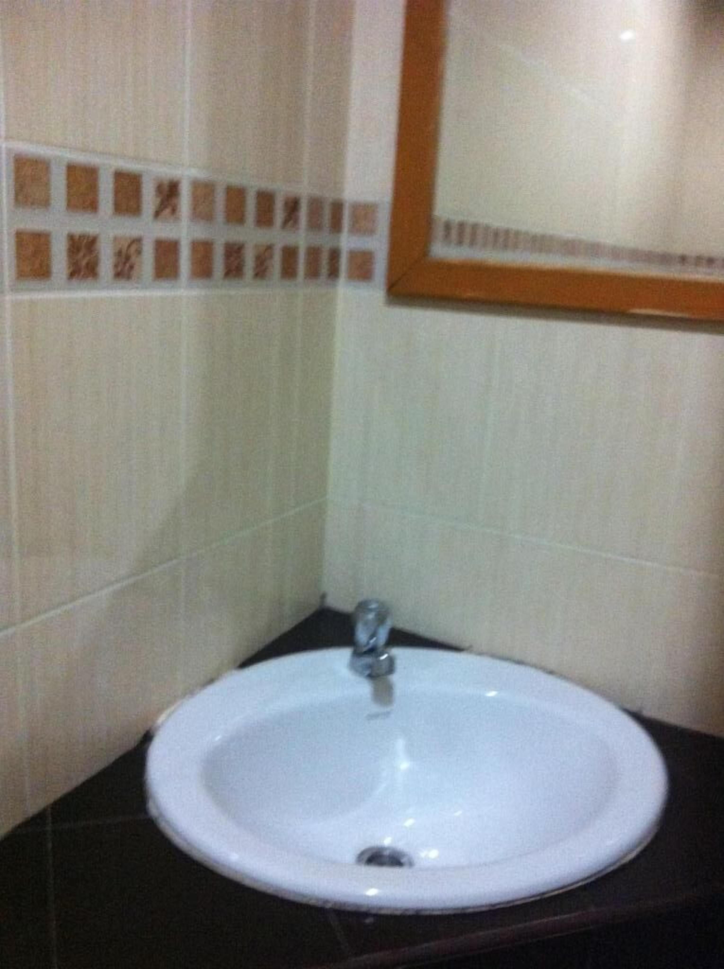 Un baño con lavamanos blanco, encimera oscura y paredes de azulejos con un borde decorativo.