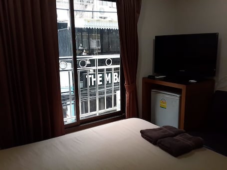 A hotel room with a bed, a television on a stand, a small refrigerator, and a window with curtains.