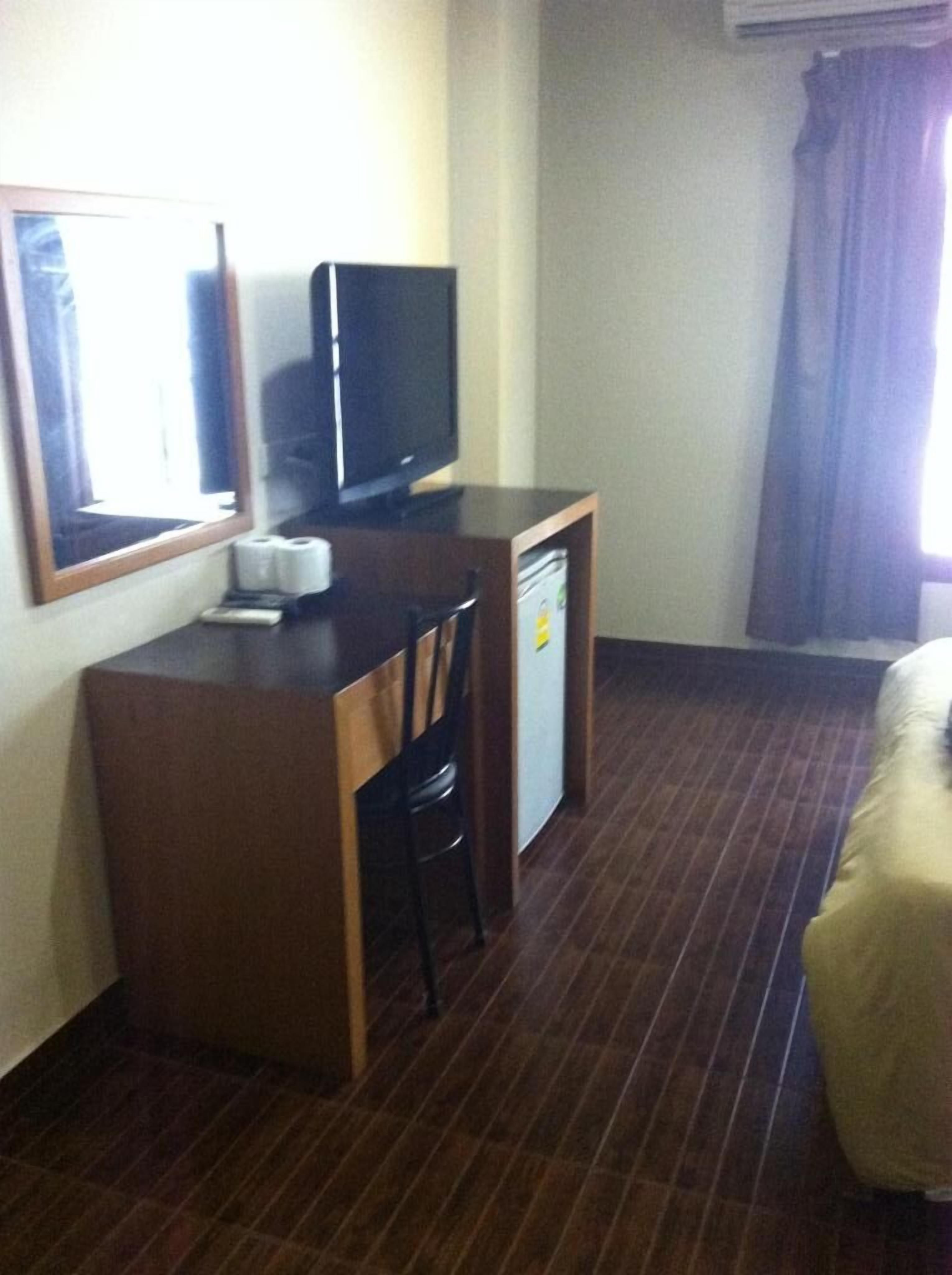 A hotel room with a wooden desk, a television, a small refrigerator, a chair, and a bed.