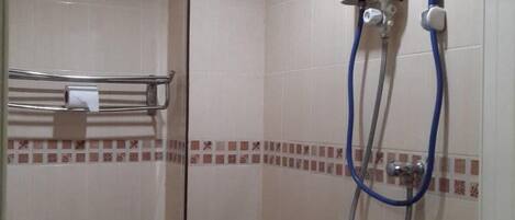 A bathroom with a toilet, a shower with a handheld showerhead, and a wall-mounted control panel.