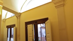 Un pasillo con techo alto, ventanas arqueadas y una puerta con paneles de vidrio esmerilado.