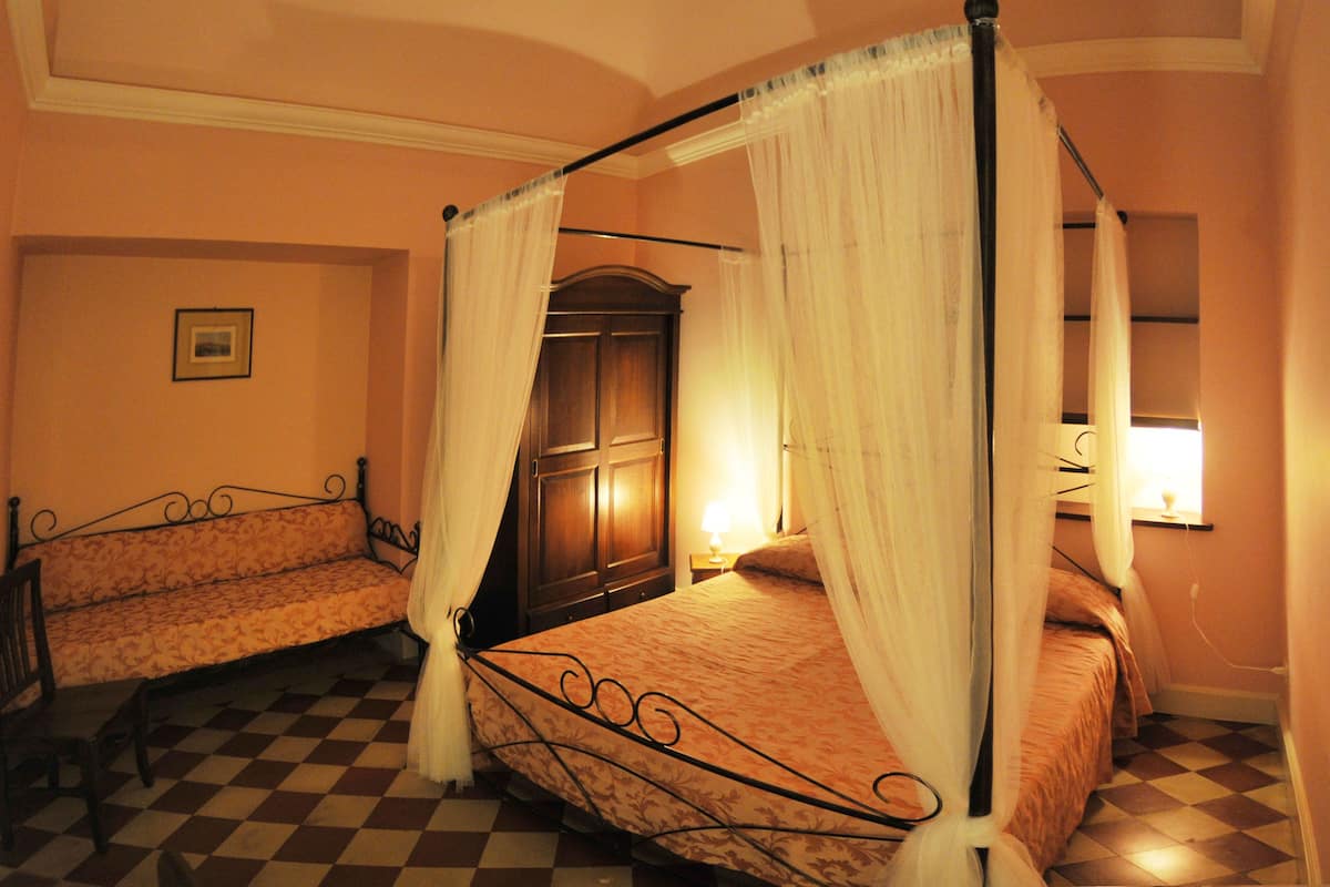 Ein Schlafzimmer mit einem Himmelbett, einer Bank und einem Holzschrank.
