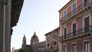 Un balcón con vista a una calle de la ciudad, que incluye coches aparcados y edificios con balcones y ventanas.