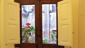 Un comedor con una mesa preparada para dos, una ventana con contraventanas abiertas y vistas a un jardín.