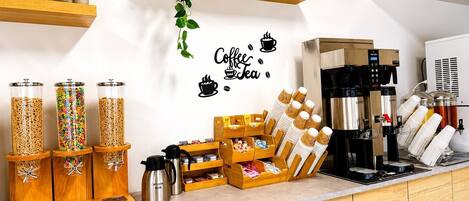 A coffee station with dispensers, a coffee machine, and a wall with a coffee and tea sign.