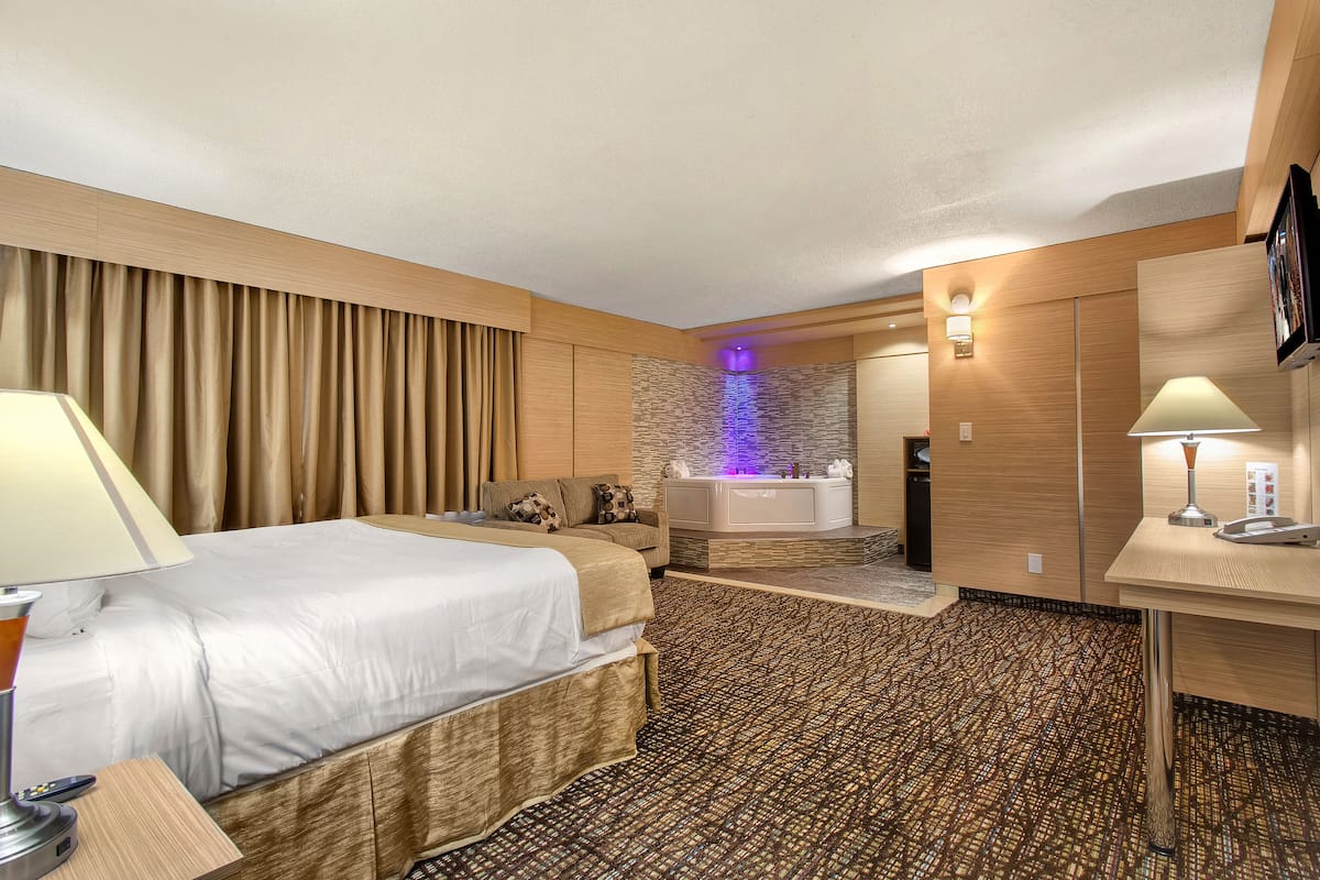 Ein Hotelzimmer mit Bett, Schreibtisch, einer Couch, einem Badezimmer mit Badewanne und einem gemusterten Teppich.