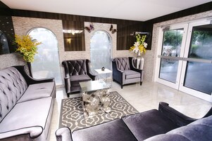 Un salon moderne avec un canapé gris, un fauteuil assorti, une table basse en verre et un vase décoratif avec des fleurs.