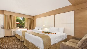 Ein Hotelzimmer mit zwei Betten, einem Schlafsofa, einem Schreibtisch und einem Fenster mit Vorhängen.