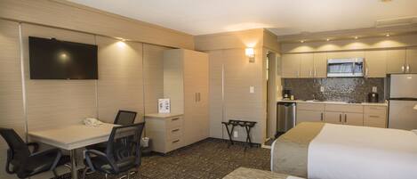 A hotel room with a bed, desk, chair, and kitchenette.