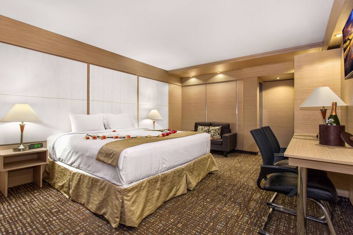 Ein Hotelzimmer mit einem großen Bett, zwei Nachttischen mit Lampen, einem Schreibtisch mit Stuhl und einer kleinen Sitzecke mit einer Couch.