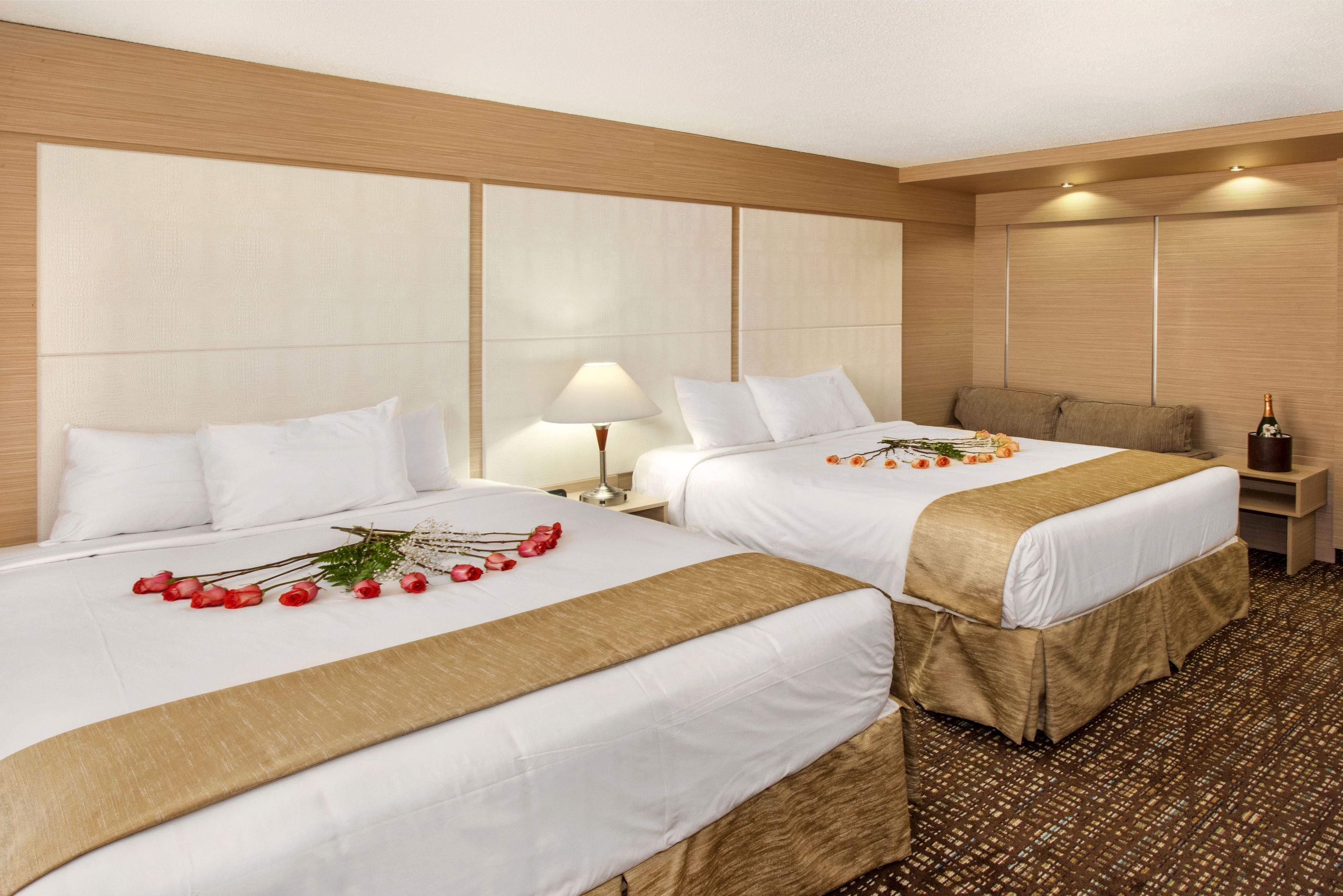 A hotel room with two beds, a nightstand, a lamp, and a bottle of champagne.