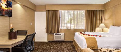 A hotel room with a bed, a desk with a chair, a TV, and a window with curtains.