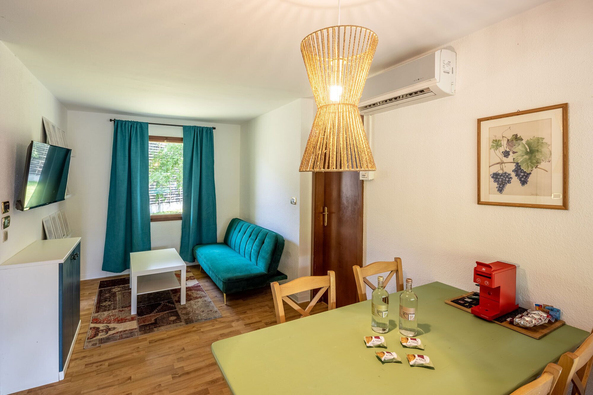 A room with a dining table, chairs, a sofa, a TV, and a window with curtains.