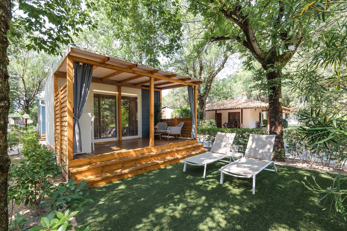 A wooden cabin with a covered porch, two lounge chairs, and a small table.